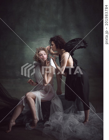 Devilish woman whispering to naive angel. Portrait of two women, angel and demon against dark, green, vintage background 101983784