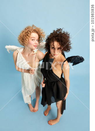 Top view portrait of beautiful young women in image of cute angel and confident demon against blue background Top view portrait of beautiful young women in image of cute angel and confident demon against blue background 101983836