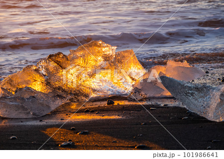Pure Ice Shining on Black Volcanic Sand at Sunset. Icebergs from Glacier in Sun Rays. Clear Ice in Ocean Waves. Famous Tourist Location in North Europe Country. Travel Destination Diamond Beach.. Pure Ice Shining on Black Volcanic Sand at Sunset. Icebergs from Glacier in Sun Rays. Clear Ice in Ocean Waves. Famous Tourist Location in North Europe Country. Travel Destination Diamond Beach.. 101986641