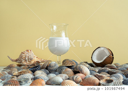 A glass of coconut milk cocktail, a coconut and seashells on a light yellow background, summer organic beverage 101987494