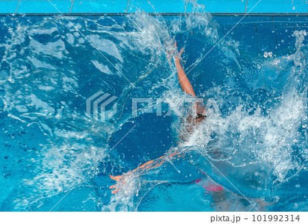 Young girl floating in blue pool water in motion among splashes of water 101992314