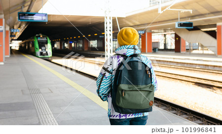 Old happy blonde woman with backpack in yellow hat waiting her train on station platform on urban background. Railroad transport concept Old happy blonde woman with backpack in yellow hat waiting her train on station platform on urban background. Railroad transport concept 101996841