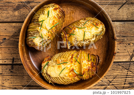 Hasselback potatoes with cheese, garlic and herbs. Wooden background. Top view Hasselback potatoes with cheese, garlic and herbs. Wooden background. Top view 101997825