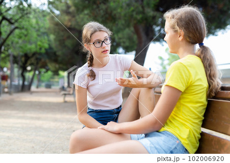 Two friendly young girls sitting on bench 102006920