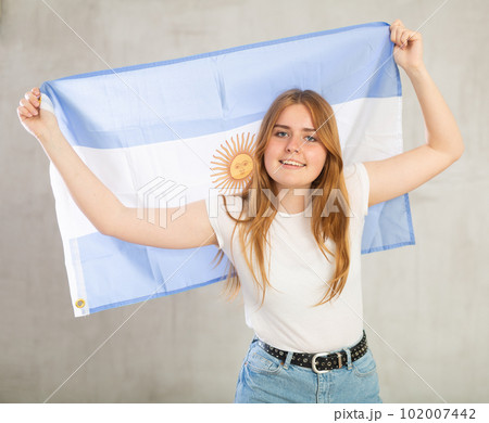 smiling girl in arms raised above head holds canvas of national flag of Argentina 102007442