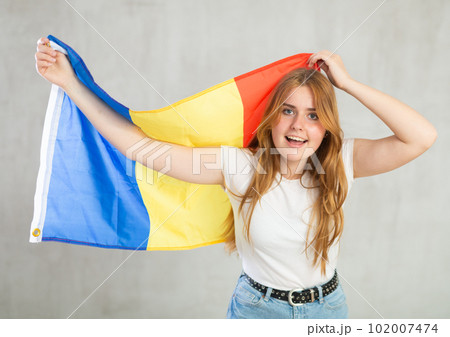 smiling girl in arms raised above head holds canvas of national flag of Romania 102007474