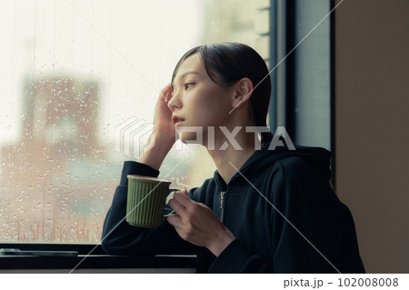 窓辺でコーヒーを飲む物憂げな顔をした若い女性 102008008
