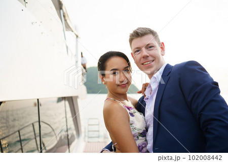 Happy Asian and caucasian couple dating on a yacht together. Lovely couple in love staying on yacht corridor and watching sunset together. Happy Asian and caucasian couple dating on a yacht together. Lovely couple in love staying on yacht corridor and watching sunset together. 102008442