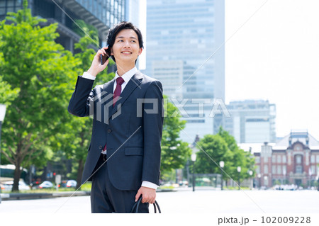 スーツ姿の新入社員の男性のビジネスマンがオフィス街でスマホを使って仕事をする スーツ姿の新入社員の男性のビジネスマンがオフィス街でスマホを使って仕事をする 102009228