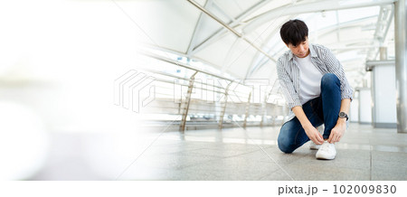 Asian young man sitting on the ground and tie a shoelaces with copyspace. A Man traveling in the city or downtown and tying a shoelace. Asian young man sitting on the ground and tie a shoelaces with copyspace. A Man traveling in the city or downtown and tying a shoelace. 102009830