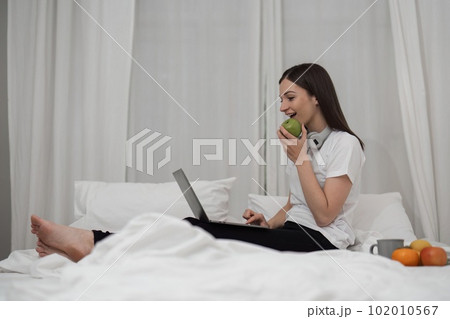 Young woman relaxing and eat fruit using laptop on checking social apps and working the bedroom Young woman relaxing and eat fruit using laptop on checking social apps and working the bedroom 102010567