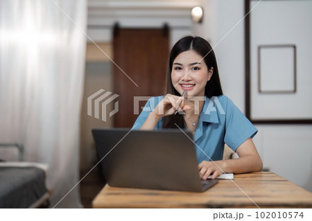 Beautiful Asian woman relaxing using laptop computer while sitting on table creative woman working and typing on keyboard at home working at home concept 102010574