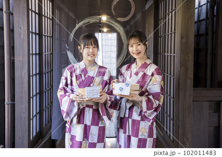 風呂桶とタオルを持ってのれんの前に立つ浴衣姿の若い女性 風呂桶とタオルを持ってのれんの前に立つ浴衣姿の若い女性 102011483