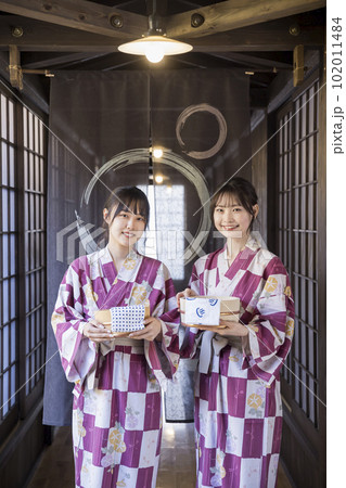 風呂桶とタオルを持ってのれんの前に立つ浴衣姿の若い女性 102011484