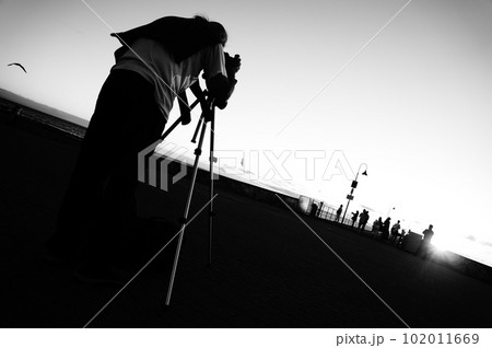 (モノクロ)海辺で三脚を立ててカメラを撮る中年男性の後ろ姿 102011669