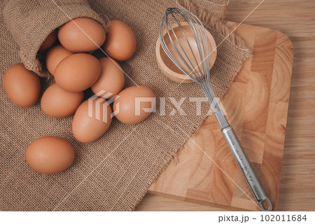 Kitchen metal wire and raw eggs on the wooden board 102011684