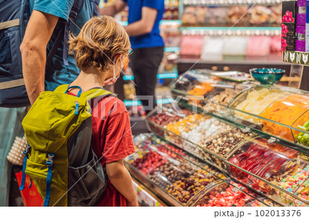 The boy looks at the counter with Turkish sweets. Traditional oriental sweet pastry cookies, nuts, dried fruits, pastilles, marmalade, Turkish desert with sugar, honey and pistachio, in display at a 102013376