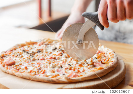 Closeup hand of chef baker in uniform blue apron cutting pizza at kitchen 102015607