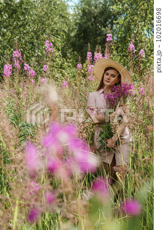 young woman in nature with a bouquet of pink wild flowers. A bouquet of Ivan-tea in the hands of a woman. 102016698