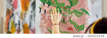 Close up shot of hand of female artist applying paint on canvas with fingers while creating abstract painting at home studio workshop 102018109