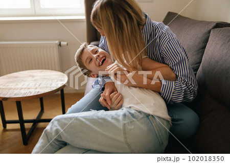 Overjoyed mother having fun with son at home, tickling and playing game on cozy couch in living room Overjoyed mother having fun with son at home, tickling and playing game on cozy couch in living room 102018350