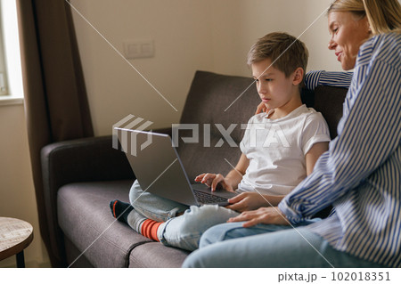Mom and son looking for something on the web, games and curious newswhile sitting on sofa 102018351