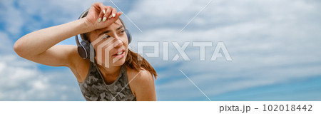 Tired female runner in headphones sweating after cardio exercise and rest after finish on beach Tired female runner in headphones sweating after cardio exercise and rest after finish on beach 102018442