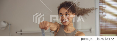 Slim woman doing exercises for hands with elastic band by online tutorials on laptop in living room Slim woman doing exercises for hands with elastic band by online tutorials on laptop in living room 102018472