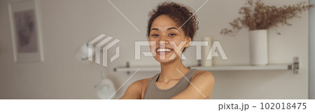 Slim woman doing exercises for hands with elastic band by online tutorials on laptop in living room 102018475