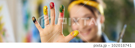 Cheerful woman smiling, creating abstract painting, applying colorful paints on canvas with fingers. Selective focus on hand in paint 102018741
