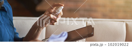 Close up shot of hands of woman disinfecting and cleaning tablet pc from microbes, viruses and bacteria with a disinfectant 102019022
