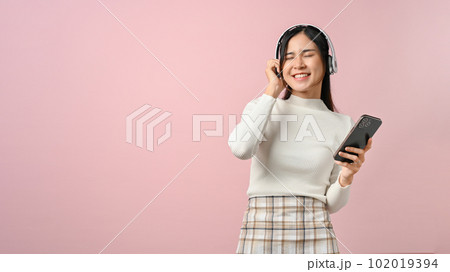 Happy young female listening to music with her headphone, on pink isolated background. Happy young female listening to music with her headphone, on pink isolated background. 102019394