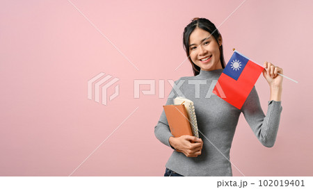Beautiful Asian girl showing Taiwan flag on pink isolated background, education concept. 102019401