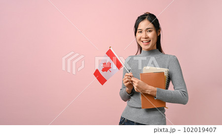 Confident Asian girl showing Canada flag on pink isolated background, education concept 102019407