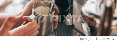 Professional barista warming milk In metal jug with steam of coffee machine 102019413