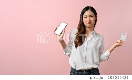 Confident Asian woman holding her smartphone and credit card, isolated on pink background 102019481