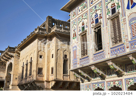 Colourful paintings and wooden windows on the outer wall of Seth Harmukhrai Sanehiram Chokhani Double Haveli, located in Mandawa, Shekhawati, Rajasthan, India 102023484