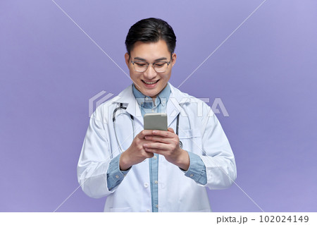 Happy doctor man texting on a smart phone isolated on a purple background 102024149