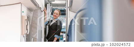 Cheerful stewardess standing at exit door in airplane Cheerful stewardess standing at exit door in airplane 102024572