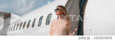Woman passenger in sunglasses standing on airplane stairs at airport and looking away 102024848