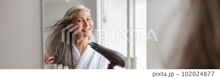 Smiling woman styling hair after taking a bath Smiling woman styling hair after taking a bath 102024877