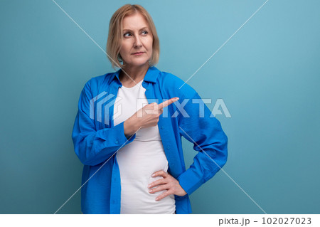 blond middle-aged woman with a bob haircut points her finger to the side in a studio background blond middle-aged woman with a bob haircut points her finger to the side in a studio background 102027023