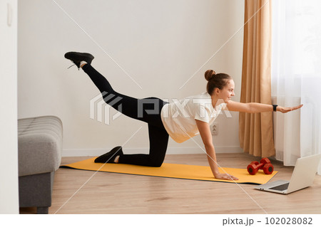 Indoor shot of athletic woman in sportswear doing yoga exercises for maintaining optimum weight and good physical, using online tutorials, having work out at home. Indoor shot of athletic woman in sportswear doing yoga exercises for maintaining optimum weight and good physical, using online tutorials, having work out at home. 102028082