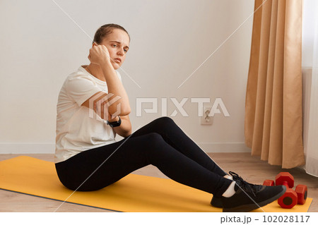 Indoor shot of sportswoman touching painful hand, sitting on mat, suffering joint injury after yoga, sport trauma elbow dislocation, muscle strain, inflamed ulnar nerve. 102028117