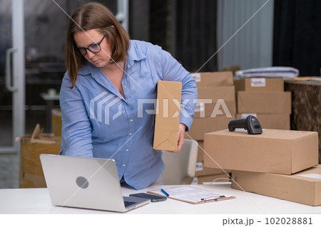 female entrepreneurs managing receipts and online orders for SMEs holding cardboard box looking to laptop, sme ecommerce online shop business. female entrepreneurs managing receipts and online orders for SMEs holding cardboard box looking to laptop, sme ecommerce online shop business. 102028881