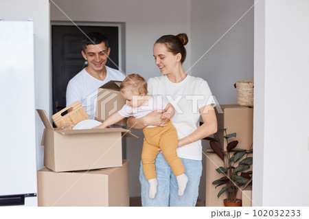 Portrait of positive happy family, mother, father and daughter posing in a new house after moving in, expressing optimistic emotions, being glad to buy or rent apartment. Portrait of positive happy family, mother, father and daughter posing in a new house after moving in, expressing optimistic emotions, being glad to buy or rent apartment. 102032233