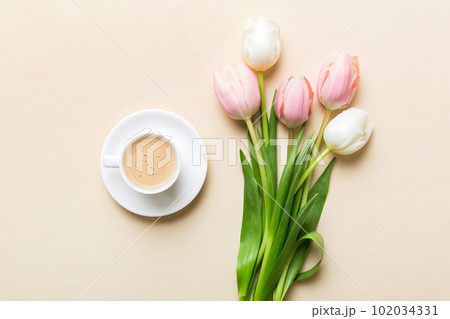 Spring background with flowers, a cup of coffee and a bouquet of pink and white tulips on colored table background with place for text. Copy space top view 102034331