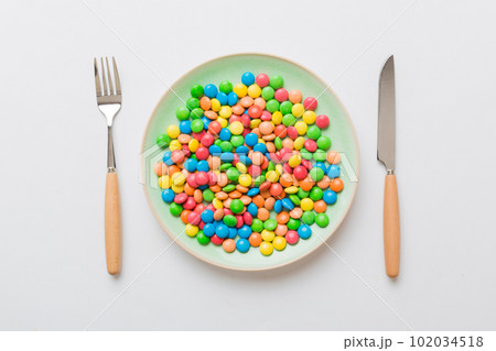 cutlery on table and sweet plate of candy. Health and obesity concept, top view on colored background 102034518