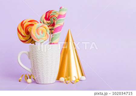 Colorful candies in cup on table on light background background. Large swirled lollipops. Creative concept of a jar full of delicious sweets from the candy store Colorful candies in cup on table on light background background. Large swirled lollipops. Creative concept of a jar full of delicious sweets from the candy store 102034715