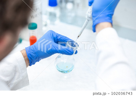 Female researcher with dropper dripping liquid into a test tube in scientific laboratory, concept of pharmaceutical environment 102036743